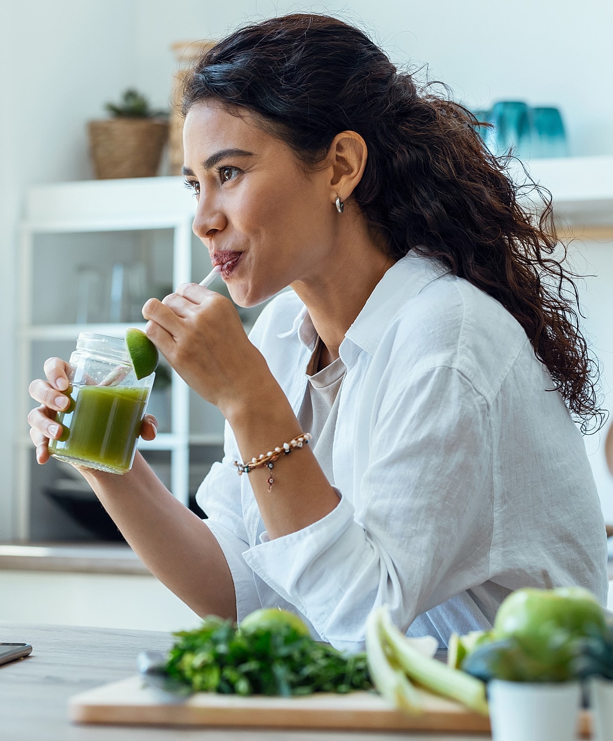 Woman enjoying a green smoothie in bright kitchen.