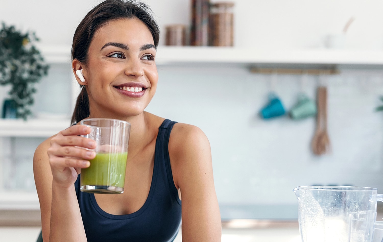 Smiling woman enjoying a green smoothie at home.