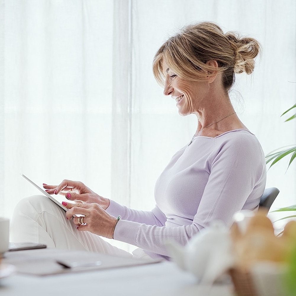 Smiling woman using tablet near breakfast table.