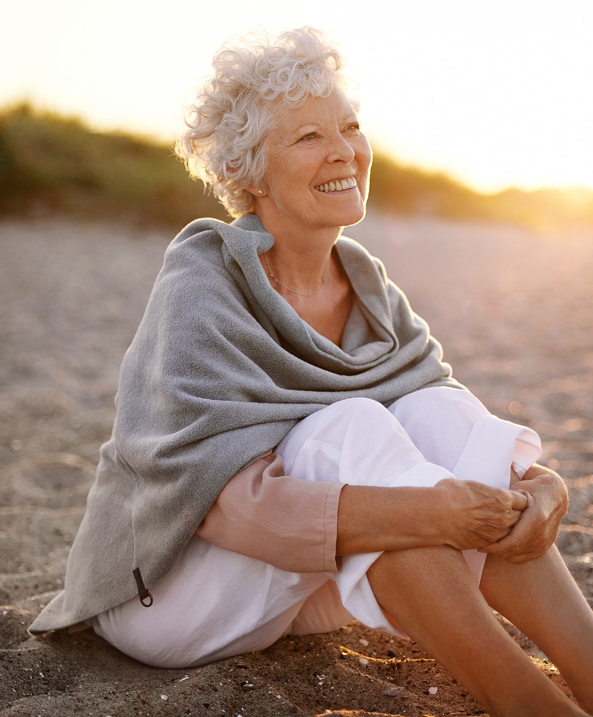 Smiling woman sitting on beach at sunset.