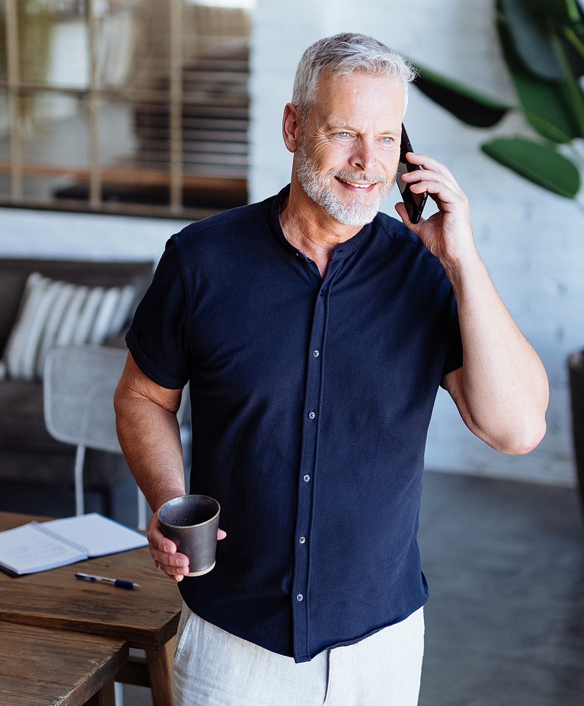 Smiling man talking on phone, holding coffee.