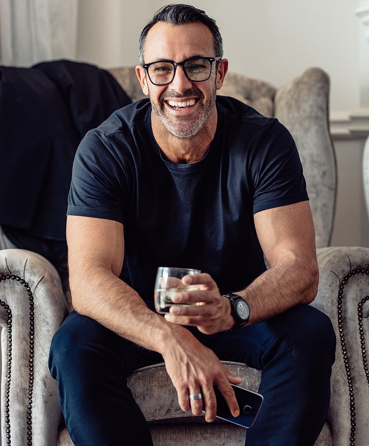 Smiling man holding a glass and smartphone.