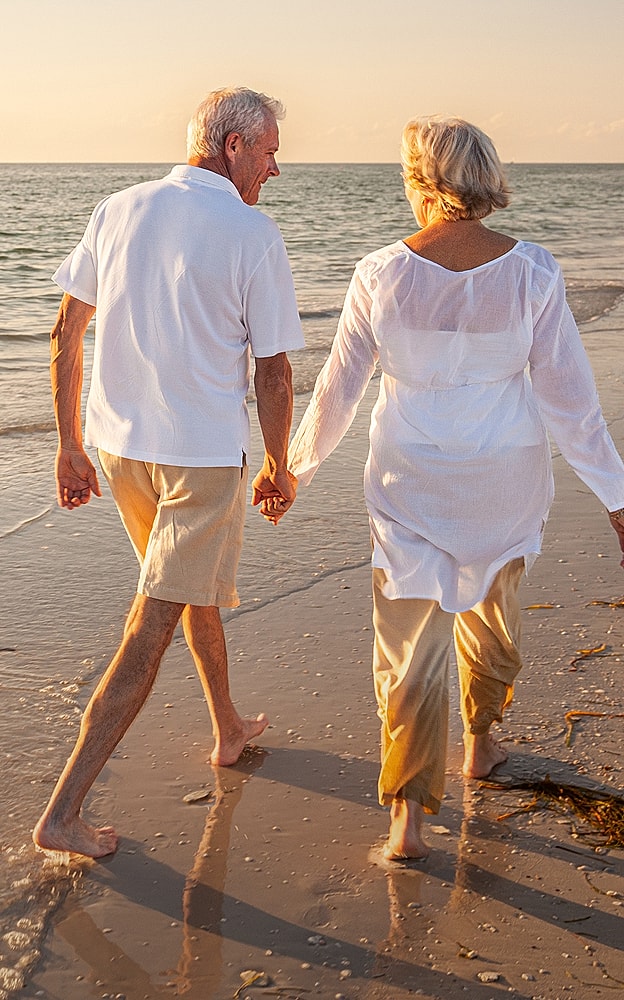 Elderly couple walking hand in hand on beach.