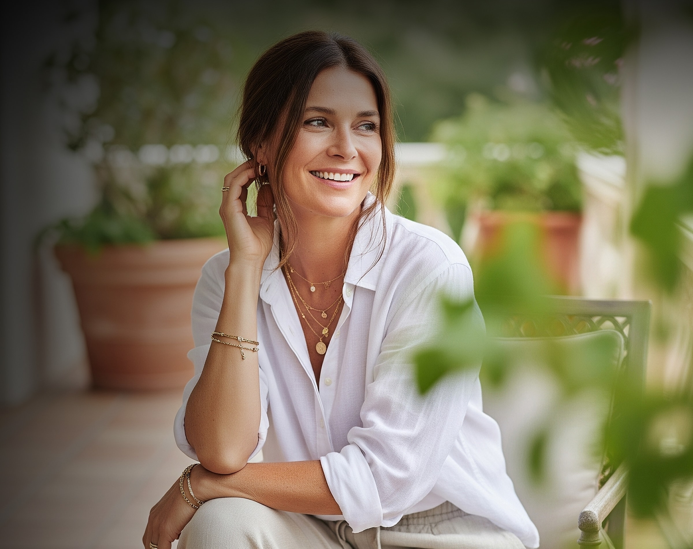 Smiling woman with jewelry in a garden setting.