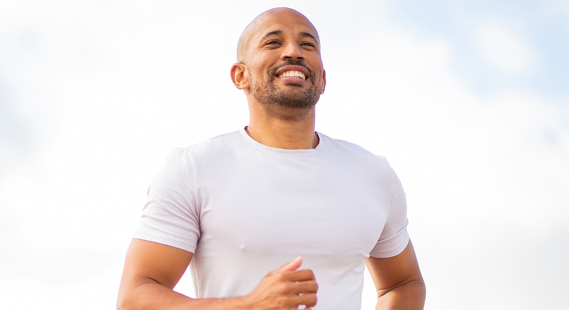 Smiling man jogging outdoors under blue sky.