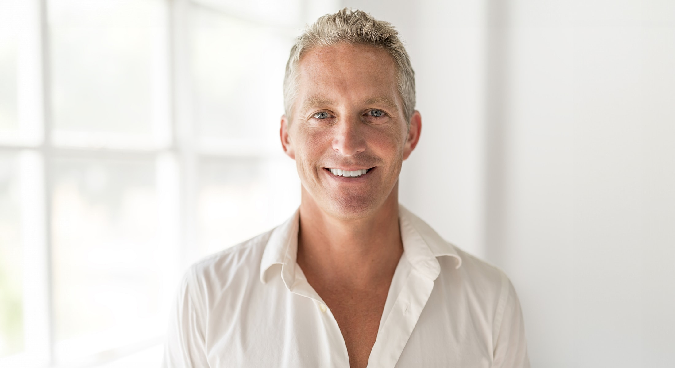 Smiling man in white shirt, natural light setting.